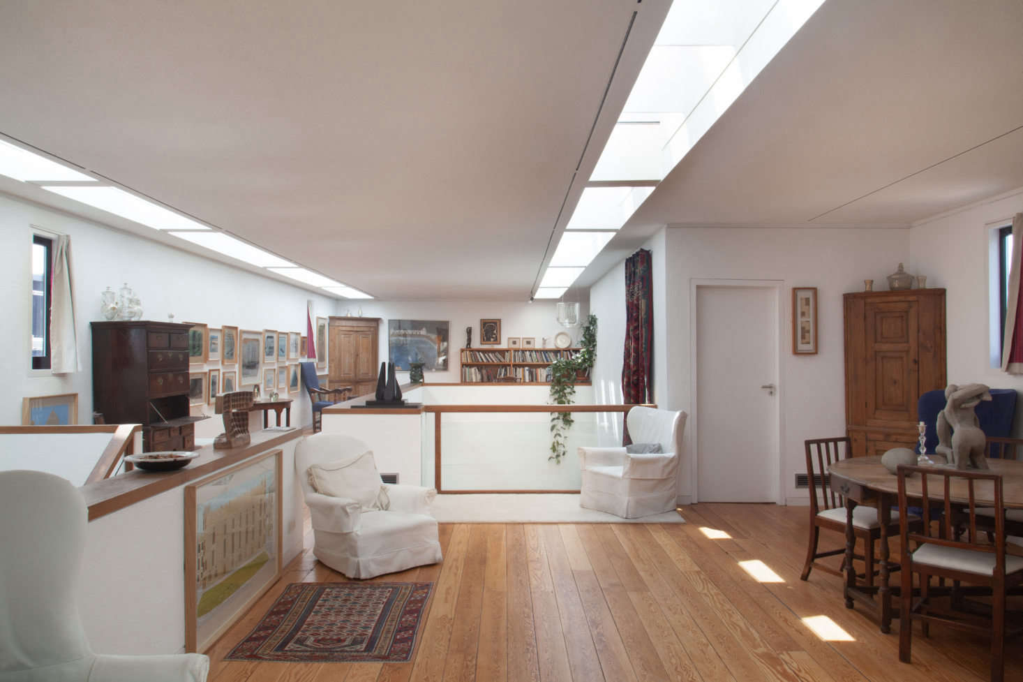 Three slipcovered armchairs are scattered down the length of the second floor modern extension. The furthest chair is tilted for viewing the low-hanging painting beneath the small window, and from the middle chair, the viewer can see Henri Gaudier-Brzeska