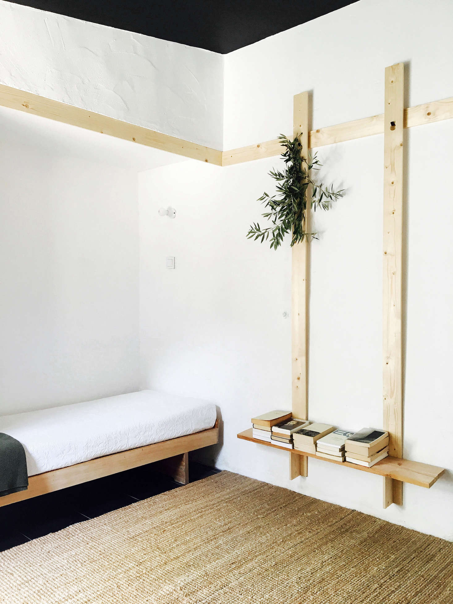 The north annex, previously a storage room, now has black-painted floors and ceilings, in contrast to the rest of the house. Here, a simple bedroom and study is trimmed in waxed wood, with a low, Shaker-like hanging shelf for books. The bakelite wall-mounted light above the bed was existing, and moved from another part of the room.
