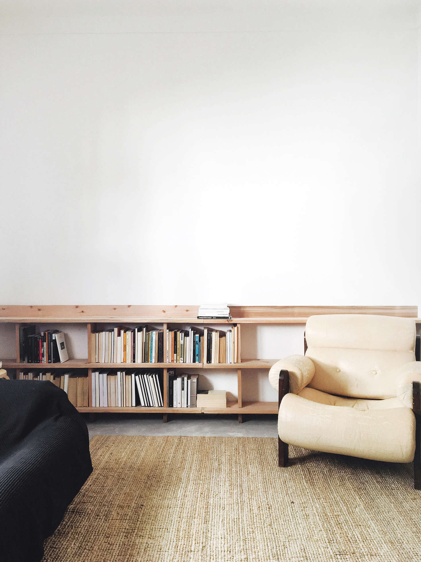 In the living area, attention is focused on the lower half of the room, with a simple woven mat and a low, waxed-wood bookshelf built into one wall.