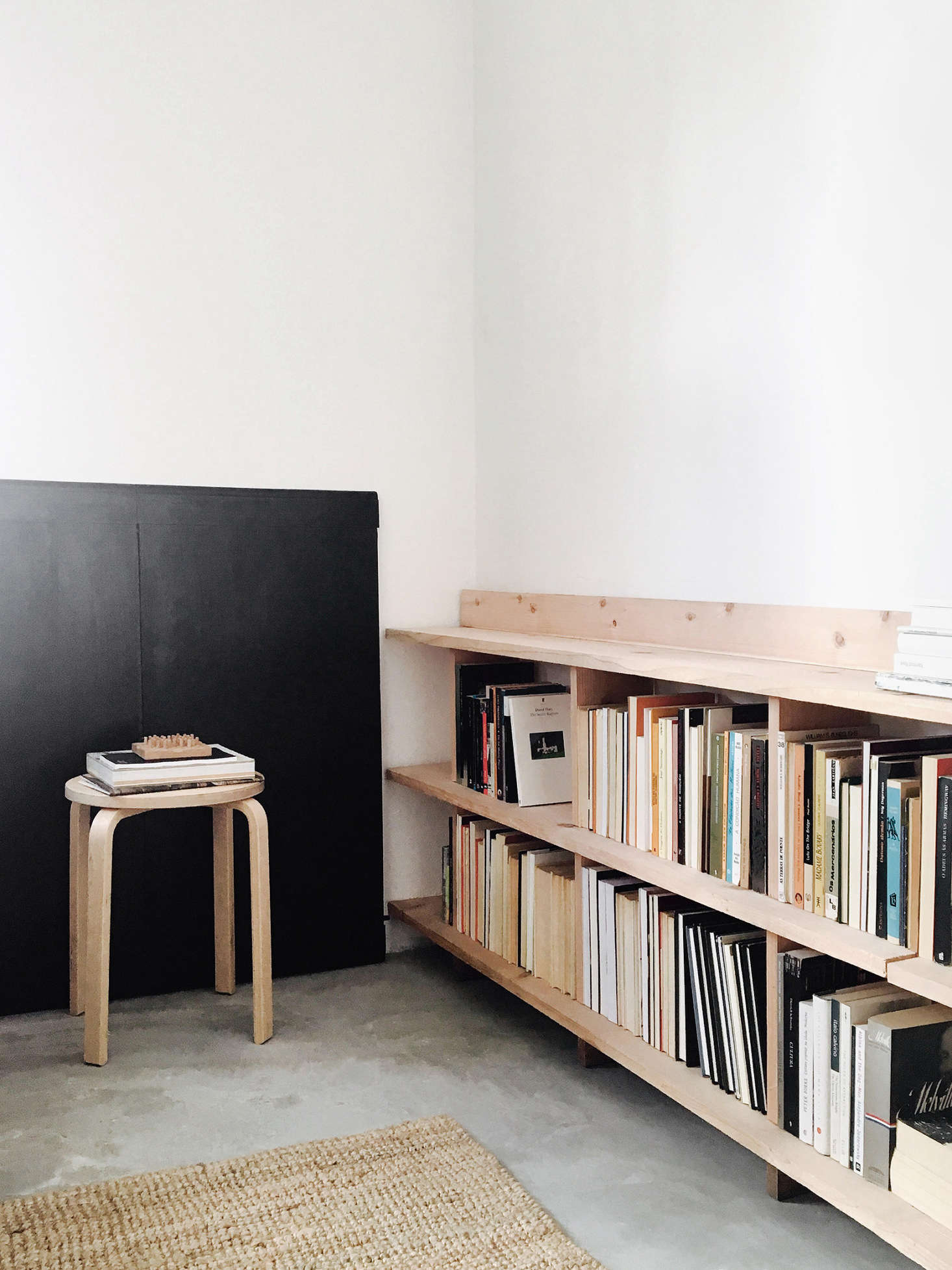 In one corner, an Alvar Aalto lookalike stool serves as an end table. Against the wall is an extension for the dining table that doubles as “vague wainscoting.”