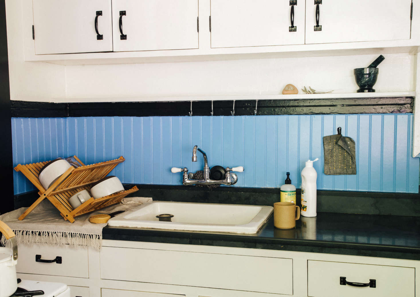 Basic nails and screw hooks above the kitchen sink hold potholders, scrub brushes, and utensils (and won
