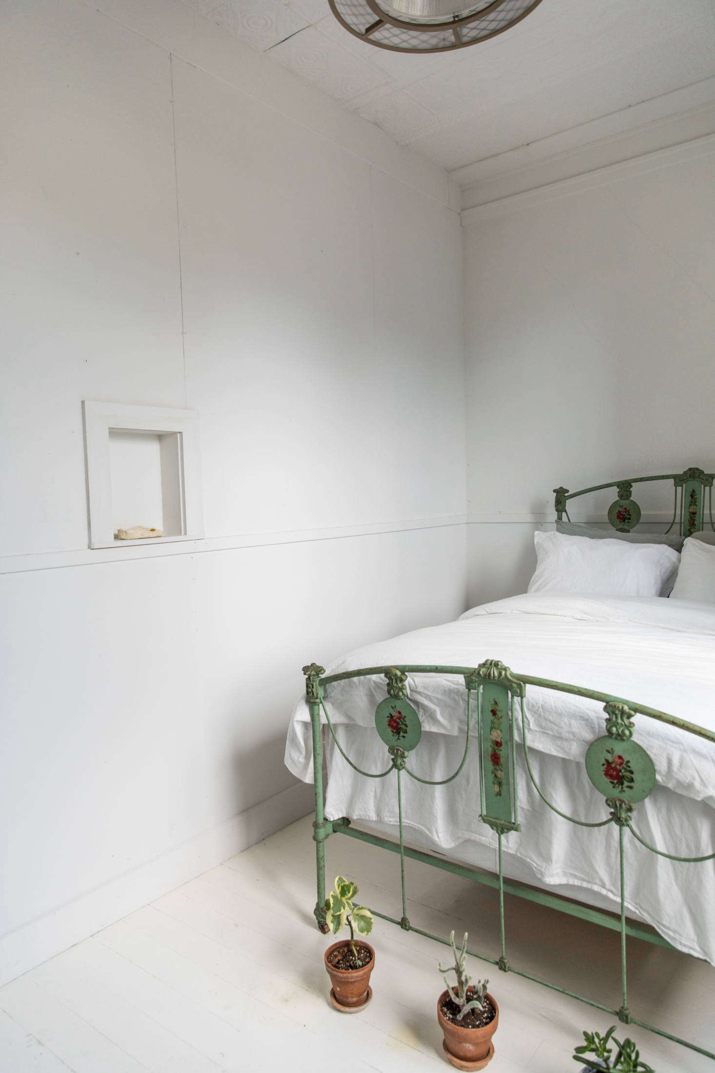 A green-hued bedroom is fitted simply, with a painted iron-frame bed that McNeil found for $75 on Craigslist. She uses the small niche in the wall to display ceramics or dried flowers.