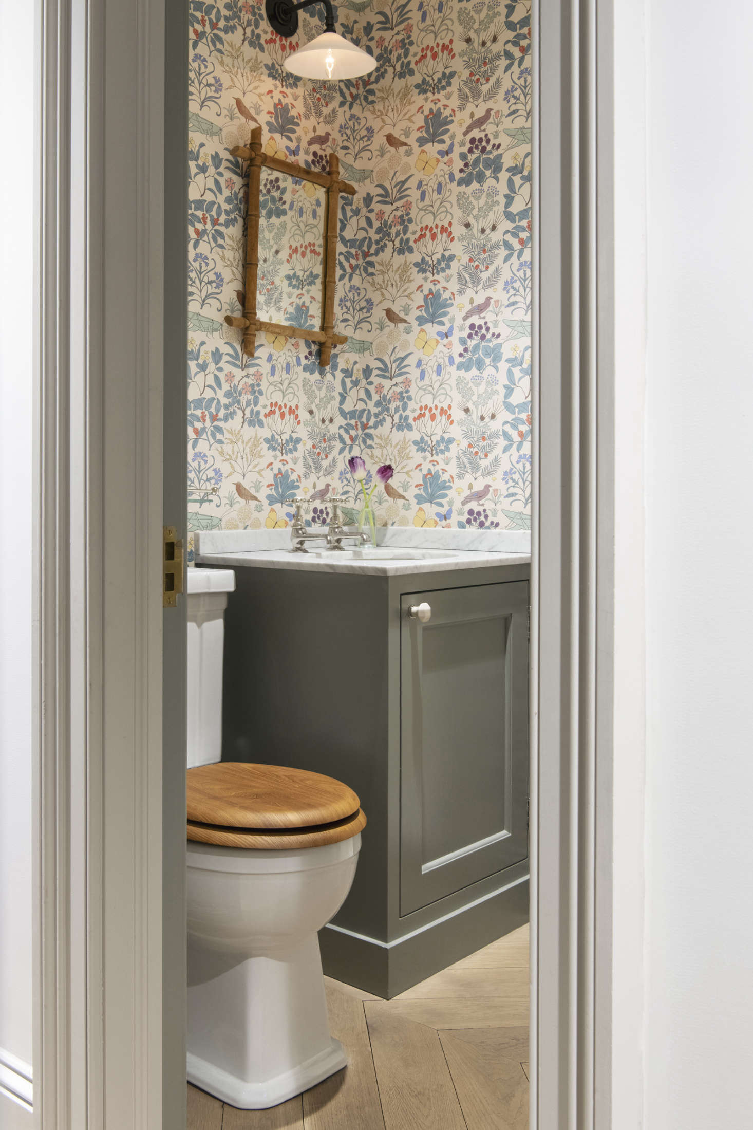 The powder room is papered in CFA Voysey’s 1926 pattern Apothecary’s Garden from Trustworth Studios. (See the same pattern in a Jersey Ice Cream Co. country house bedroom.) The sconce over the mirror is the Glass Wall Light from Hector Finch.