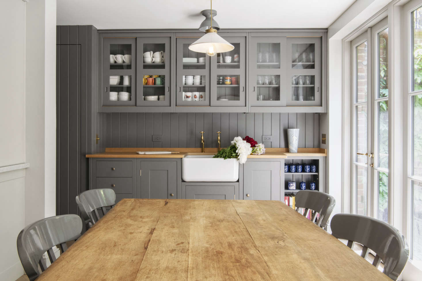 The butler’s sink counter is adjacent to a beadboard-paneled mudroom. The counter is Plain English oak butcher block. The gray ceramic ceiling light is the Alabax from Schoolhouse Electric.