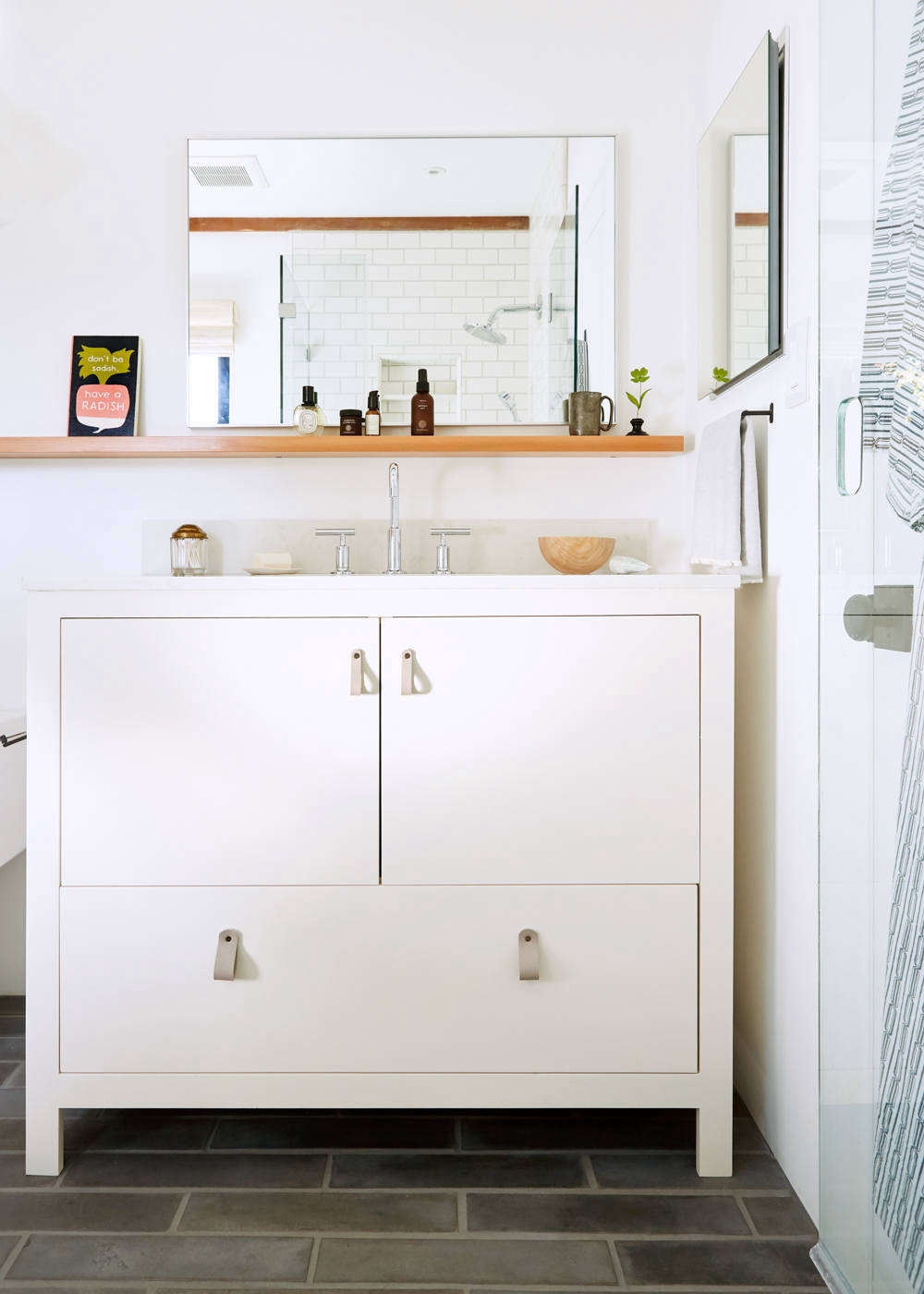 Look closely and you’ll see that the shower door has an oval cutout pull: “The space between the vanity and shower door is not terribly wide, so I spec’d a cutout in the glass to avoid a protruding handle.” The sink console was made by Alfredo Garcia of H & H Cabinet in Oakland and painted in Farrow & Ball Dimity. The gray leather loop pulls are from 3 Twenty Leatherworks, and the sink fixtures are Kohler Purist in polished chrome. The sink counter is IRG Pental Quartz in Lattice. The 24-by-36-inch Infinity Mirror mounted over the sink is from CB2.