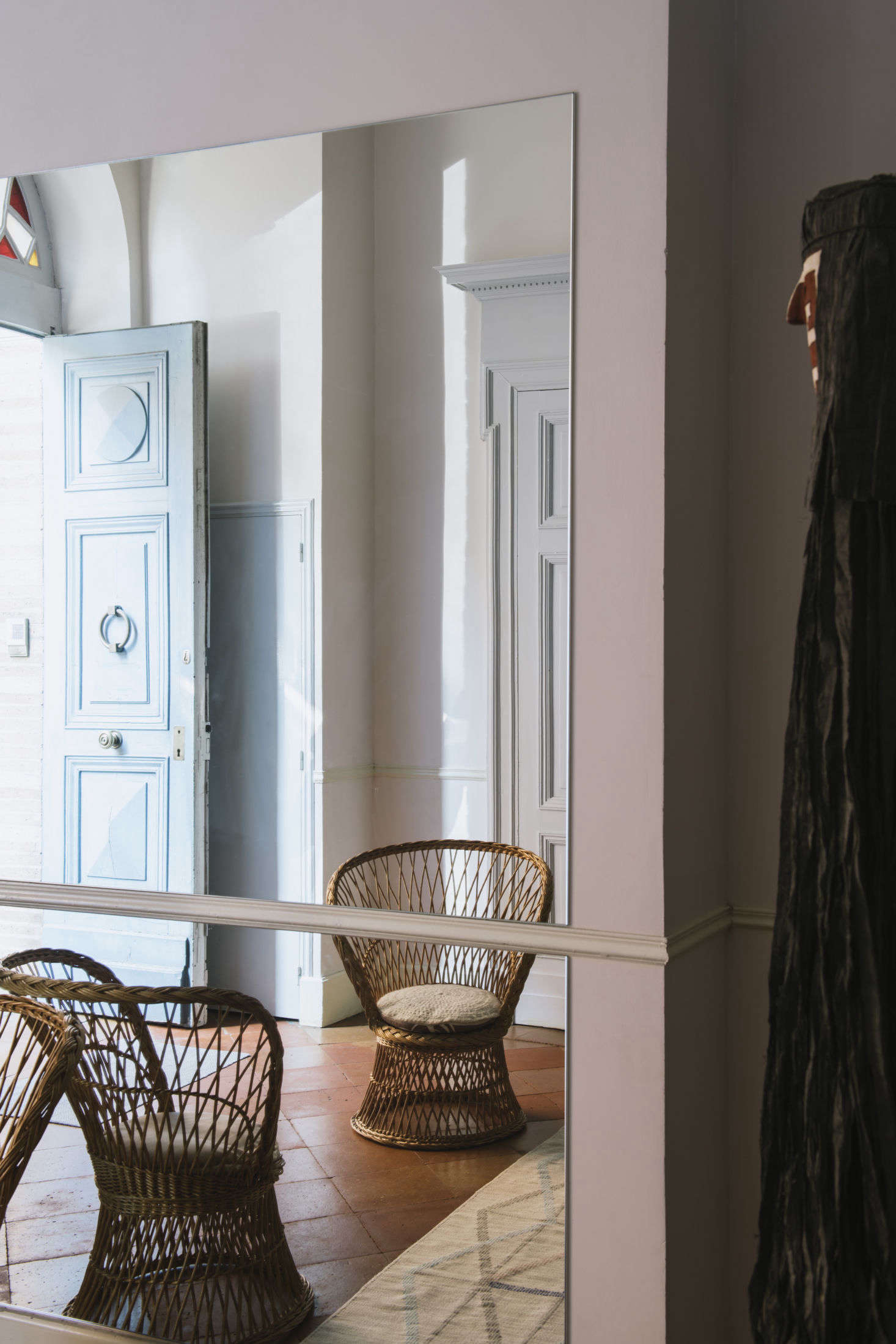 Stepping into the house, entrants are greeted by a cheerful blue door, a rattan chair, and panels of mirrors.