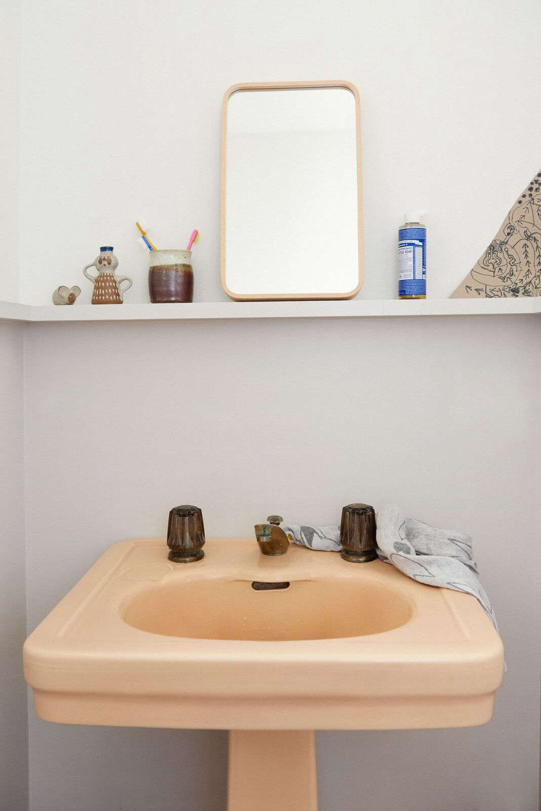 In the powder room, Lena plays with scale, opting to lean a petite mirror on a ledge instead of installing a full-sized one. The peach-colored pedestal sink was a Craigslist find.