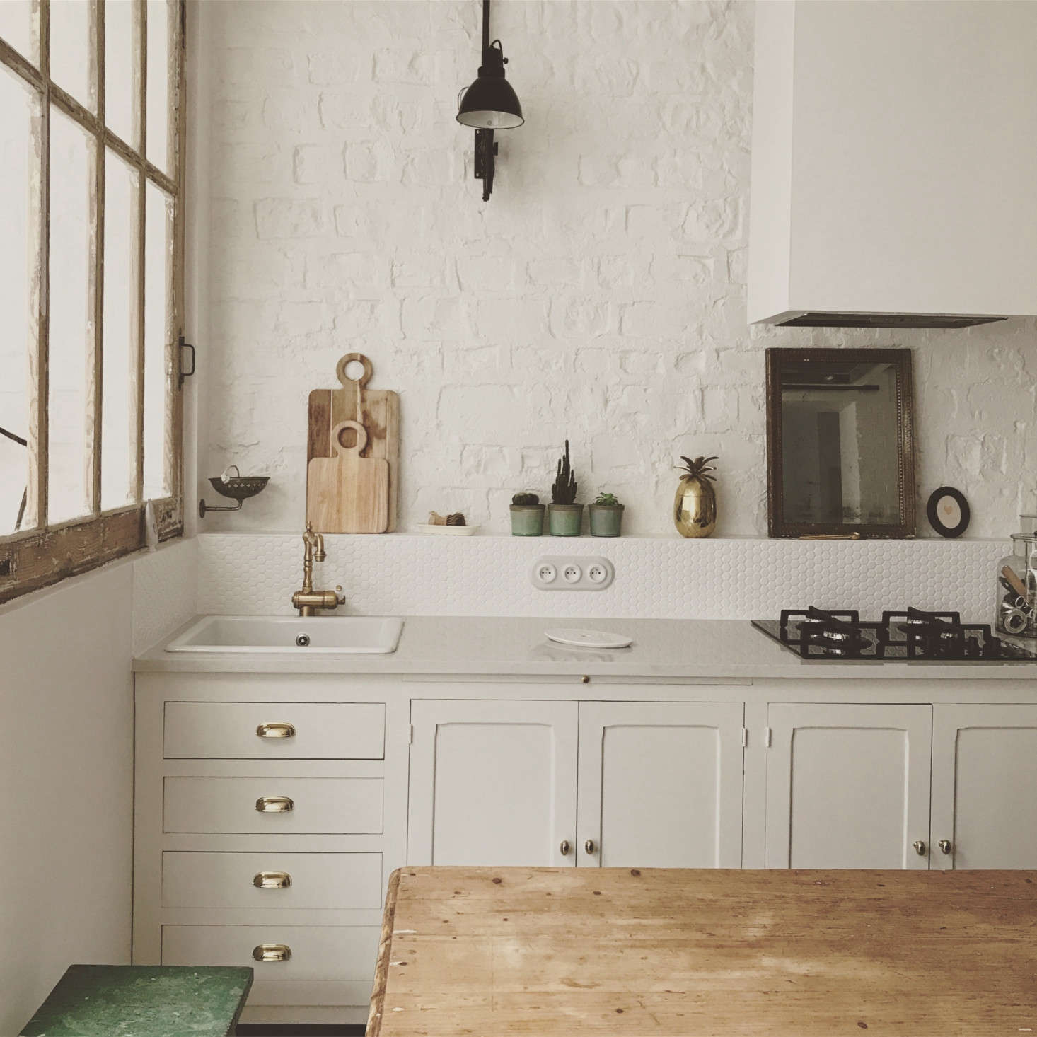 A coat of white paint on the exposed brick freshens up the space. A few unexpected moments: a single black accordion sconce and an antique mirror as backsplash behind the stove.