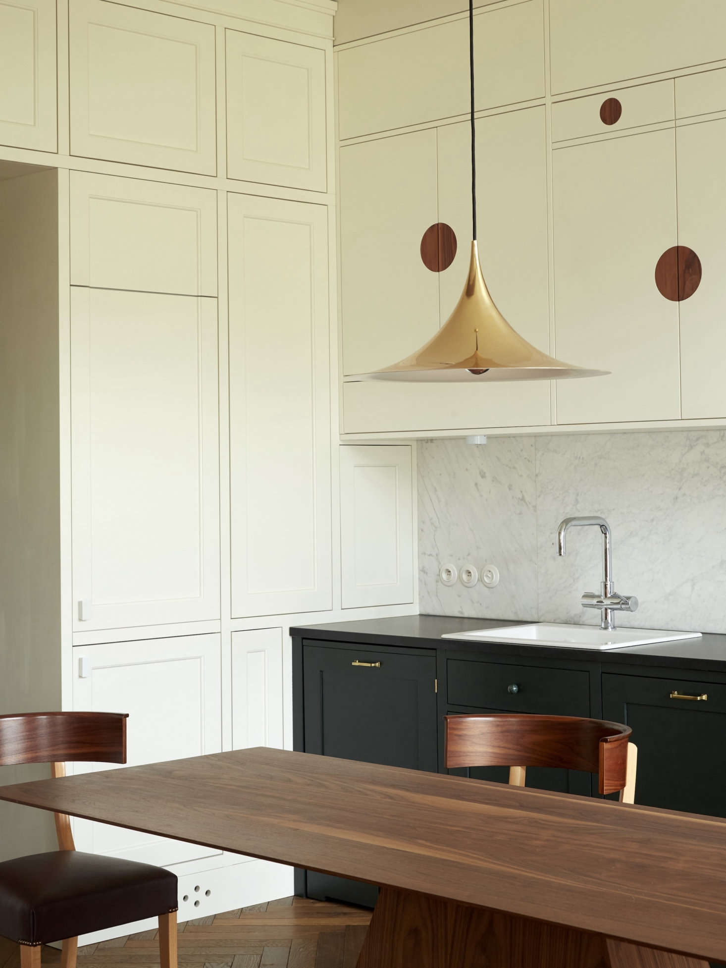 While the upper cabinets have a whimsical look, the lower cabinets, painted Farrow & Ball Studio Green, are traditional. The brass Semi Pendant light is by Gubi.