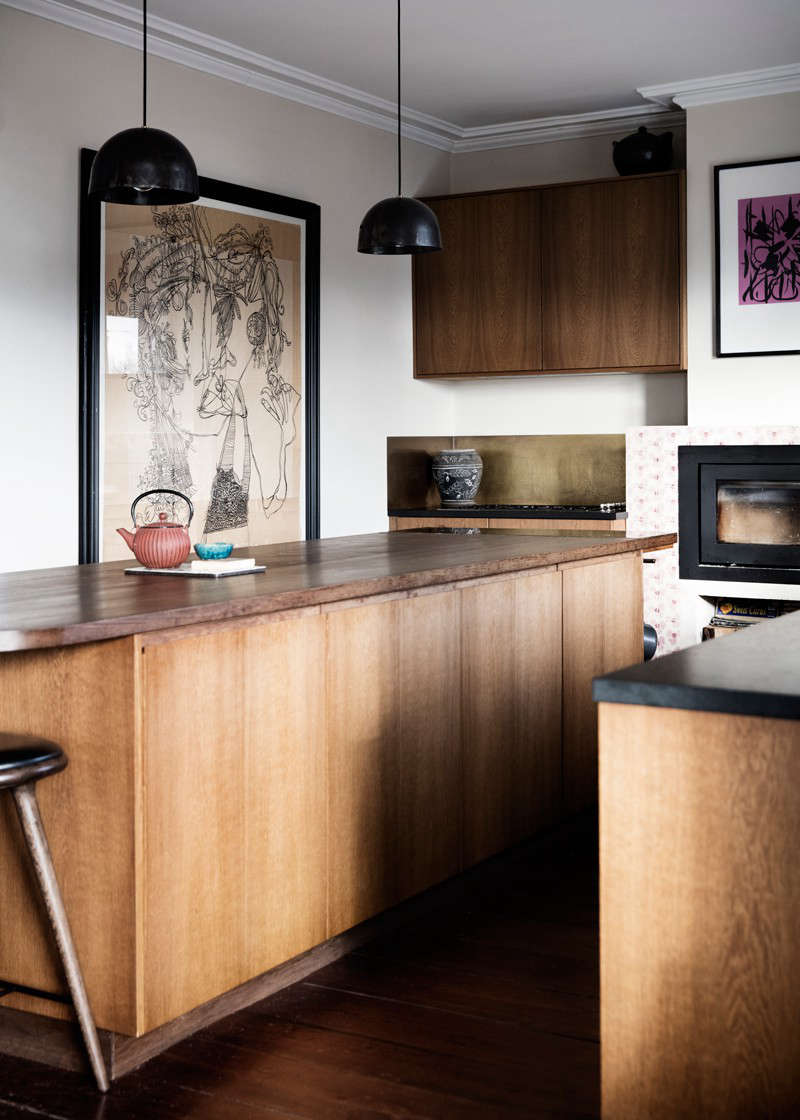 In the back corner, the stove and cooktop are set off by a patinated brass backsplash. The couple selected a variety of drawings and paintings to display. To those concerned about grease and grime, Rebecca says, “everything near the stove and fireplace is behind glass. We think it’s important to ‘use’ art.”