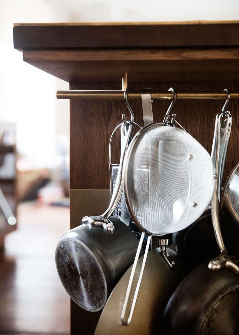 Challenged to find space to hang pots and pans and kitchen tools, the designers inserted a brass rod under the deep counter and detailed the island with a tall brass toe kick.