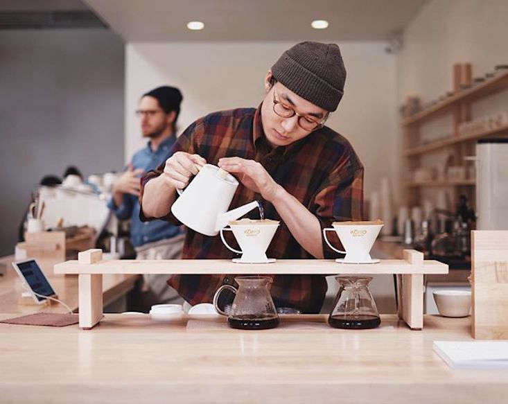 A barista brews coffee using Kono drippers and Kalita glass carafes, both Japanese brands.
