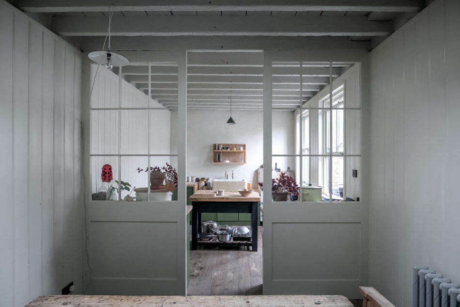 A more pulled-back view into the kitchen. The sash windows, exposed ceiling joists, and tongue-and-groove paneling on the walls lend the semi-open space a rustic look.