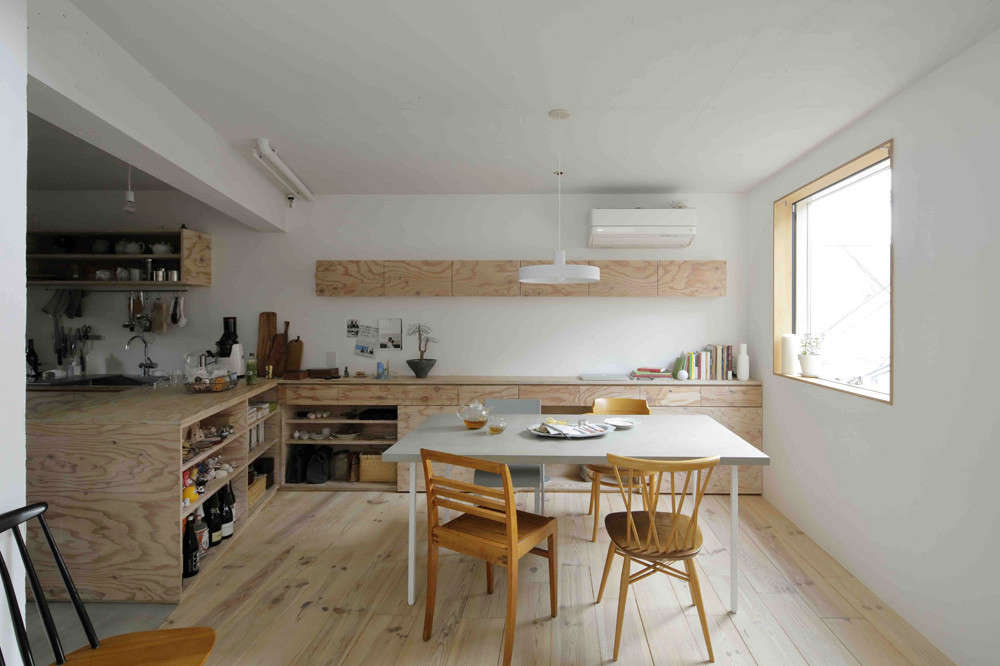 The kitchen—with two long counters that extends out from the sink—opens to a combination eating area and living room set off by wide-board pine flooring. No. 555 designed the concrete-topped table and surrounded it with an odd lot vintage chairs. The narrow cabinet on the back wall contains Mio