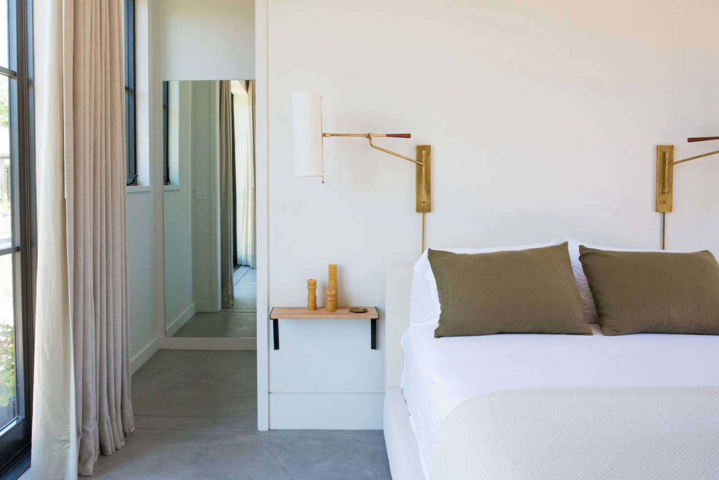 A guest bedroom, with olive-colored pillows found at Napa Valley Vintage Home and a pair of Frankfort Articulating Wall Sconces.