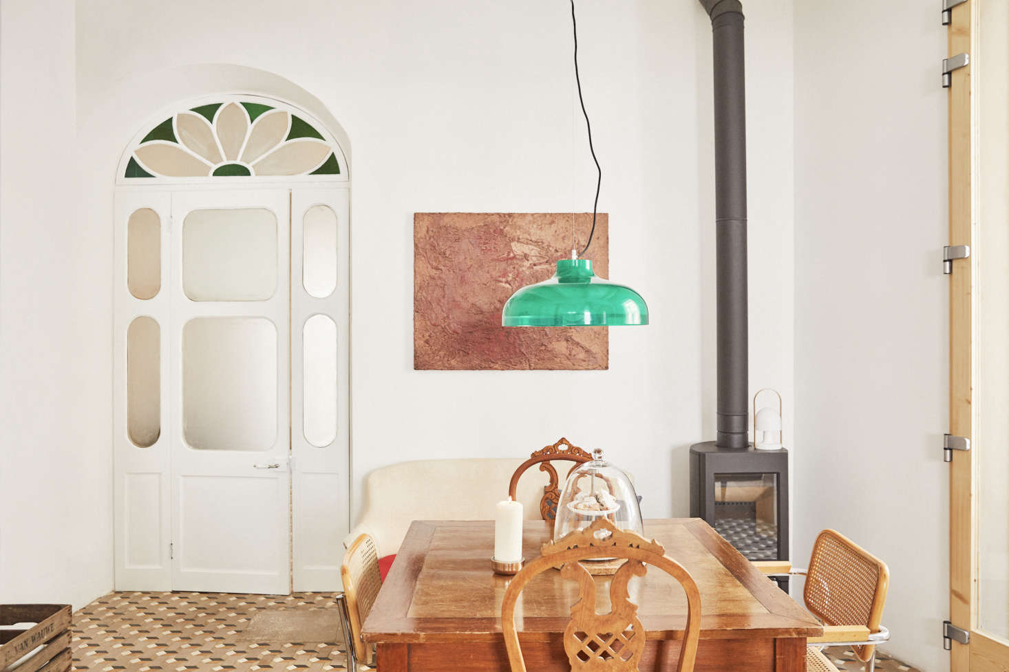 A dining area with an old farm table, high back antique chairs, and vintage Breuer Cesca Chairs. Hanging above is vintage light in green (for something similar, see our post Easy Pieces: Colorful Glass Pendant Lights and the Kartell Fl/y Suspension Light).