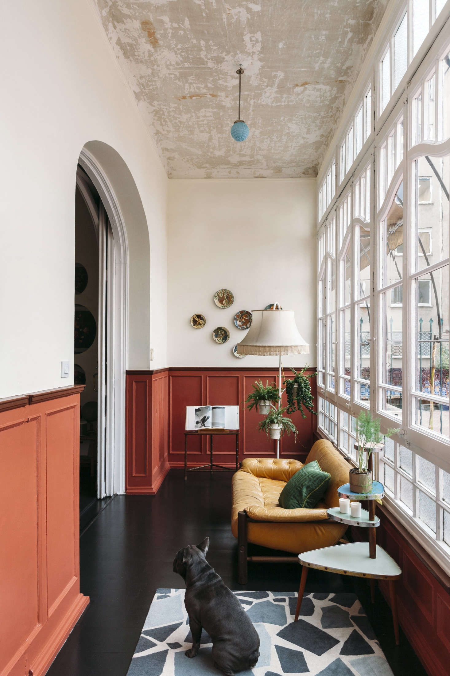 An arched entry leads to a long, narrow lounge with its original divided glass wall and a refinished ebonized floor. The designers scraped away the ceiling paint and left it as is, detailed with a small blue milk glass pendant.