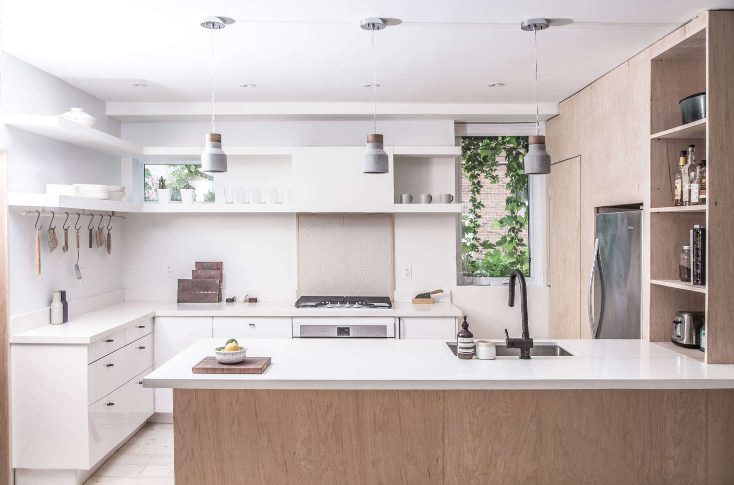 The refrigerator is fitted into the plywood volume but left undisguised. The range has a tiled backsplash and the two-tiered overhead shelves conceal the exhaust fan.