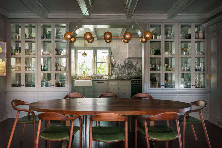 A wall of glass cabinets, which can be accessed from both sides, separates the kitchen from the dining room. The dining table is from BDDW, the Neva chairs are by Artisan, and the Trapeze ceiling light is by Apparatus.