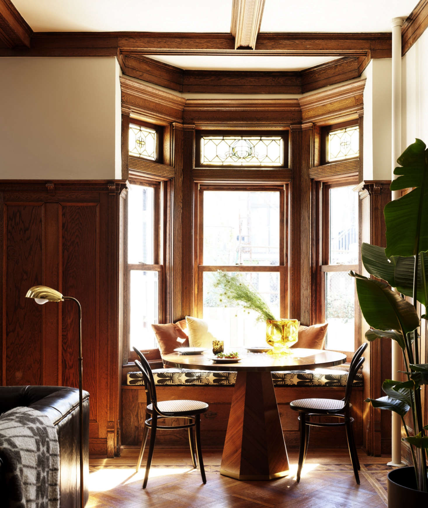 Caned chairs flank a breakfast table, set into a bow window. The stained glass at the tops of the windows is original.
