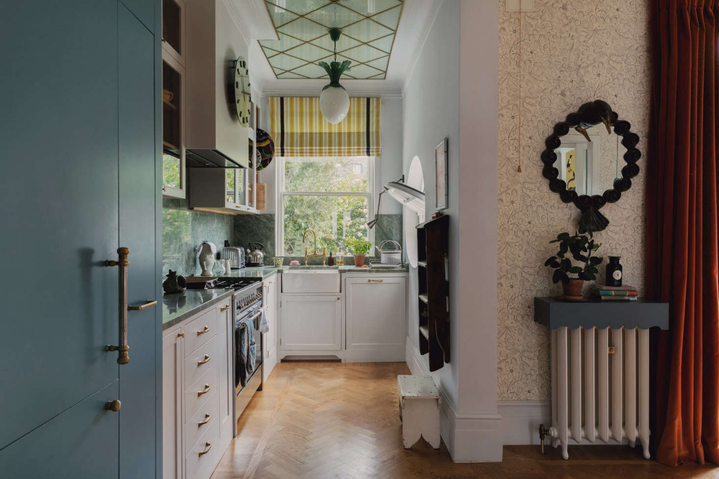 Because the dining room is attached to the kitchen, Heuman disguised the refrigerator (at left) as a blue armoire. The kitchen is tiny but efficient and organized (note the hanging step ladder). “Although my interiors use print and color, we also think a lot about how to design an environment that is practical to live in, where items can be stored away and a sense of calm can be created.” The Dodo Egg pendant light is by Heuman.