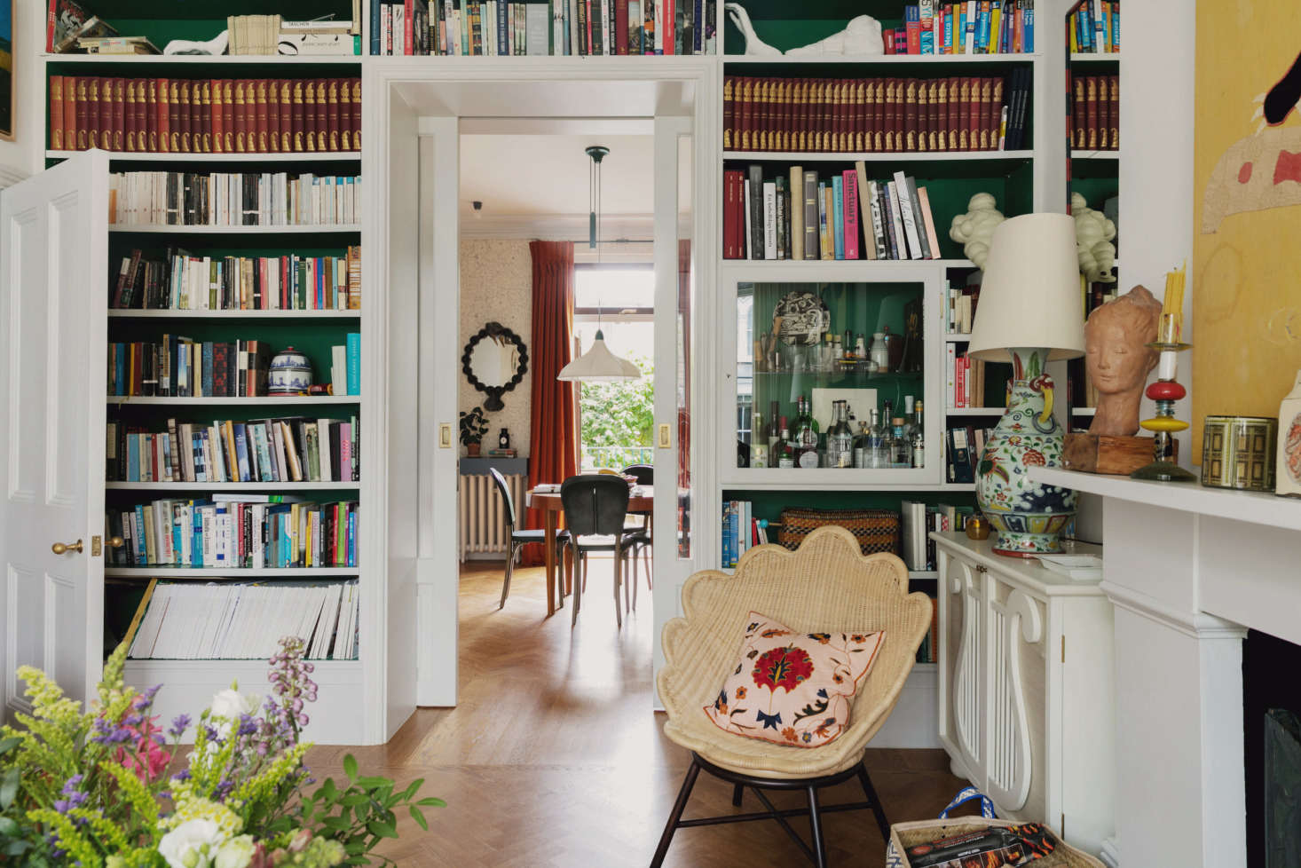 The view from the living room into the dining area. “I have nothing against an organized, refined aesthetic, but I love color and pattern too much to ever live in a completely pared-back environment,” says Heuman. The scalloped rattan chair is by Soane Britain. The bookshelves and Lire Cabinet (at right) are both Heuman designs.