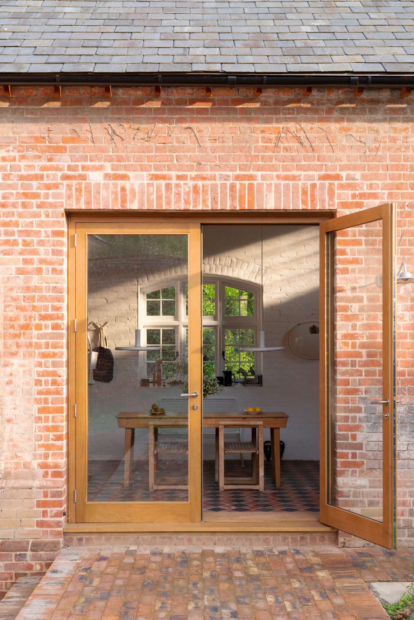 Glazed double doors framed in oak open to a brick terrace and walled garden. The grocer who once used the building as a storeroom planted tomatoes that Sandy says “still sweetly and stubbornly grow out back.”
