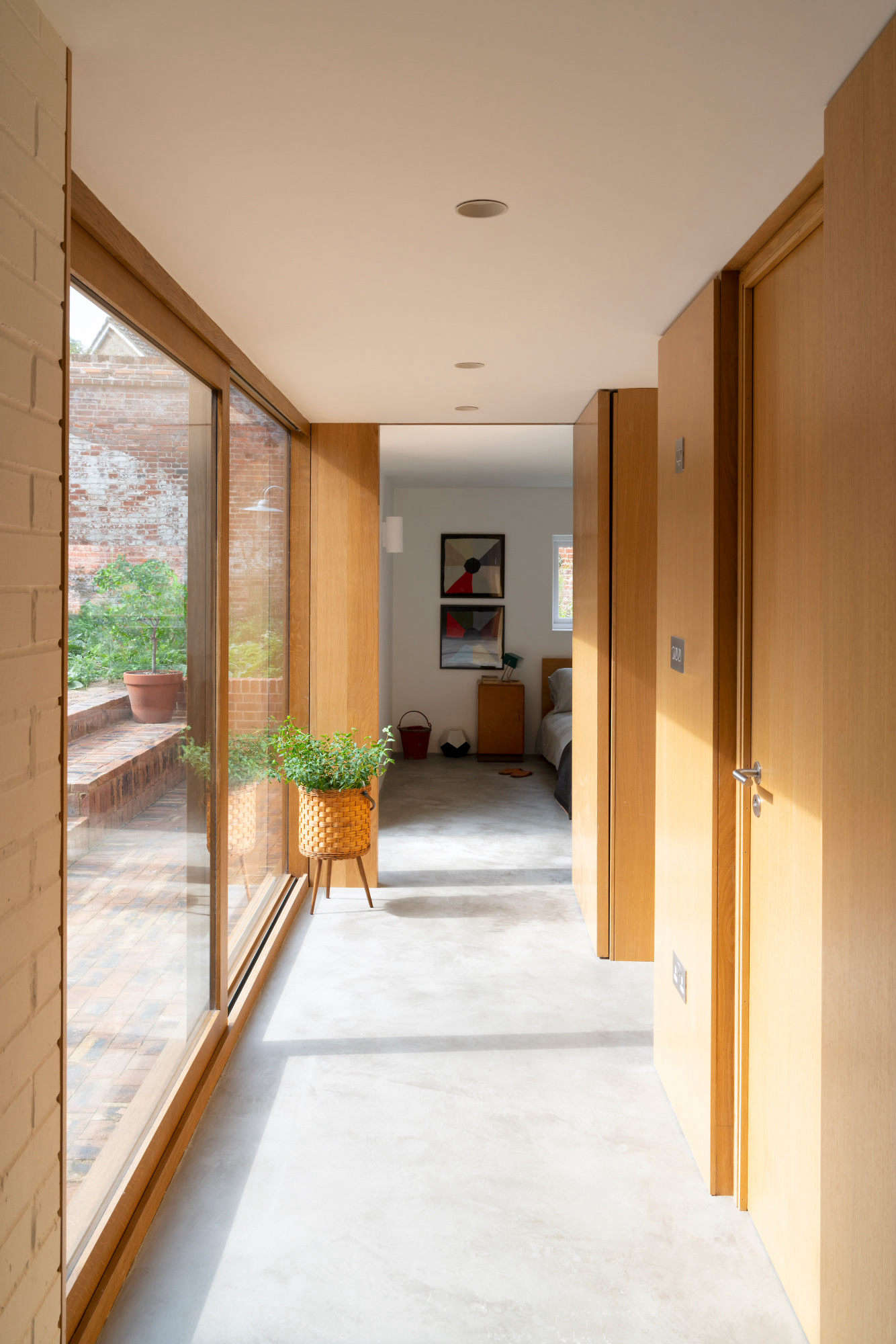The addition’s glazed hallway overlooks the garden. Deben Joinery did all of the woodwork: shown here, walls and doors in oak. The floor is micro-concrete. “I wanted the extension to look like a new addition and not a pastiche of the original building,” says Sandy, “but they have things in common: simplicity and good light.”
