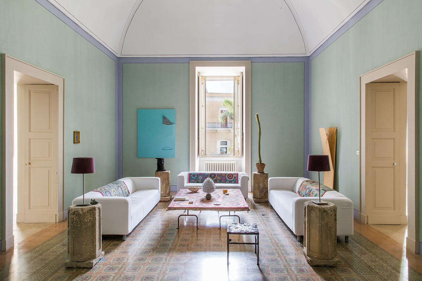 The symmetrical living room in the hotel’s Suite Apartment has eggshell-blue walls, an unexpected periwinkle trim, original mosaic floors, and sculptural furnishings.