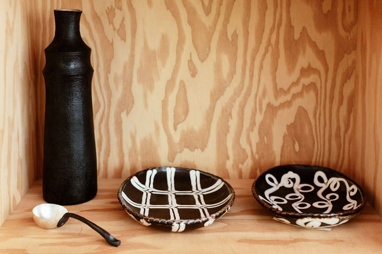 The room’s plywood shelves are devoted to “shared storage” between the kitchen and study. Shown here, a stoneware Ruth vase by Mirena Kim and slipware bowls by Tenshin Juba.