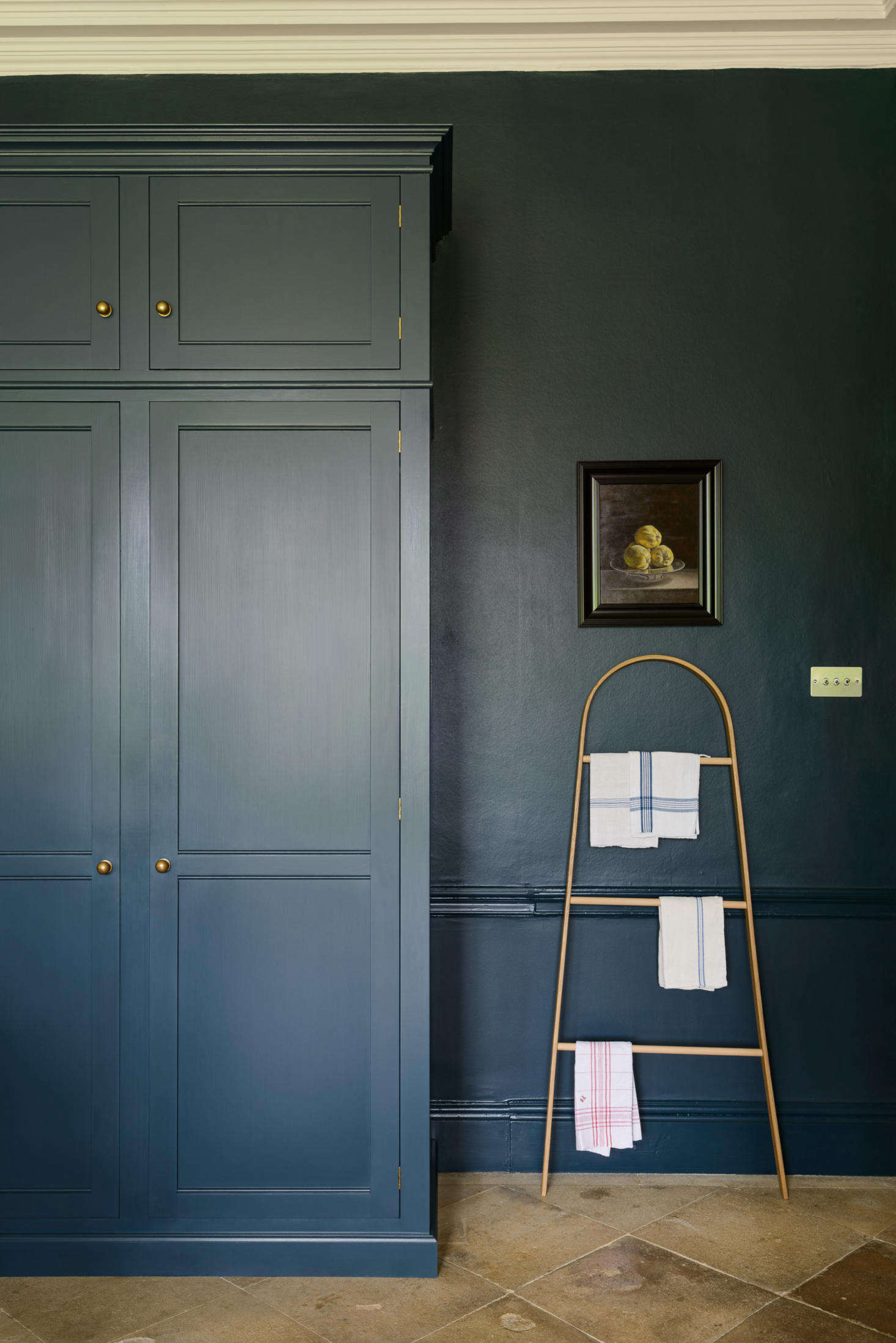 The wall of cabinets ends with high cabinet doors that conceal the refrigerator and pantry. Kitchen linens hang from the Taffrail rack by Tom Raffield.