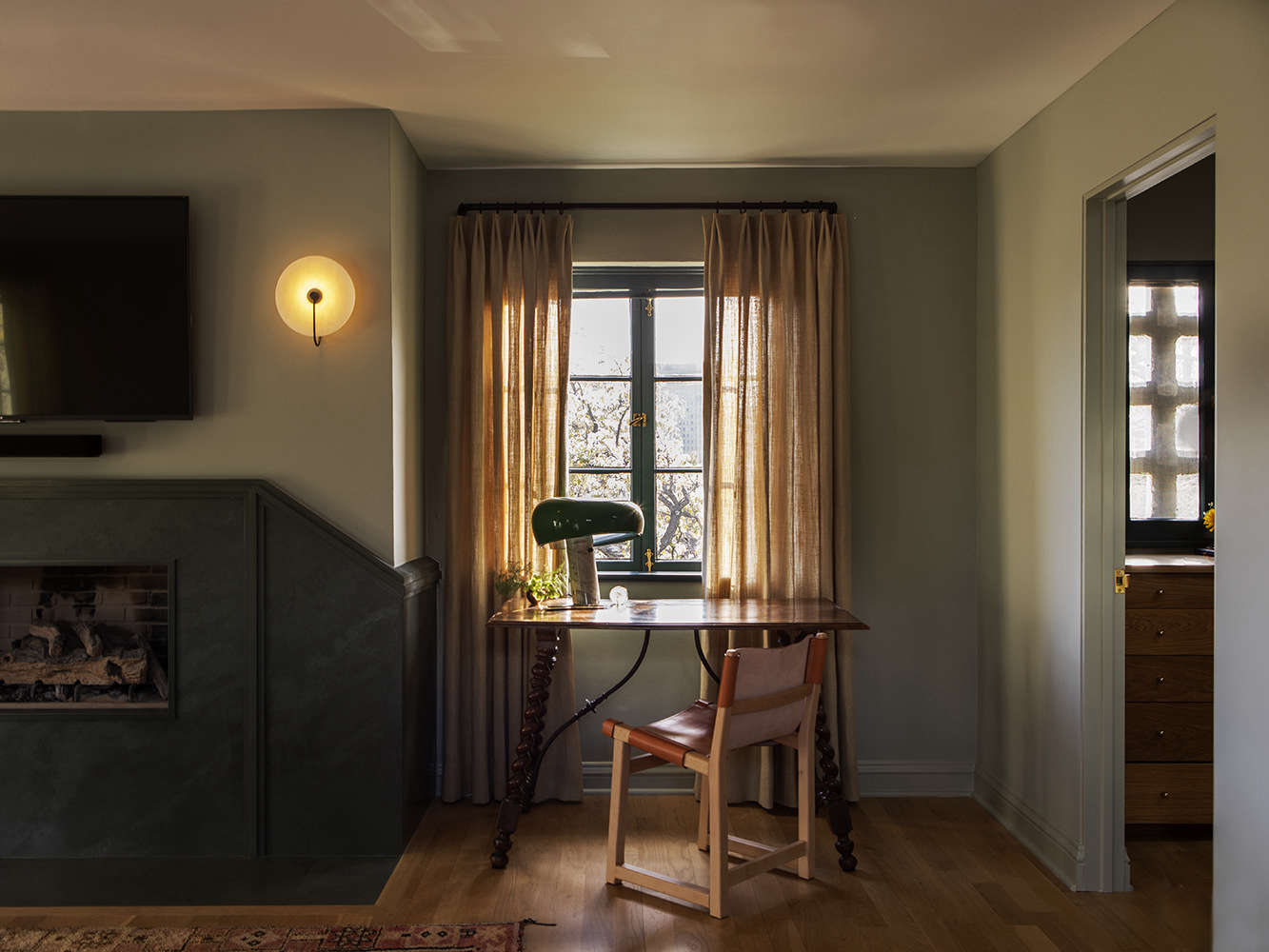 A vintage desk with a Castiglioni Snoopy lamp stands next to a new wraparound mantel of green slate.