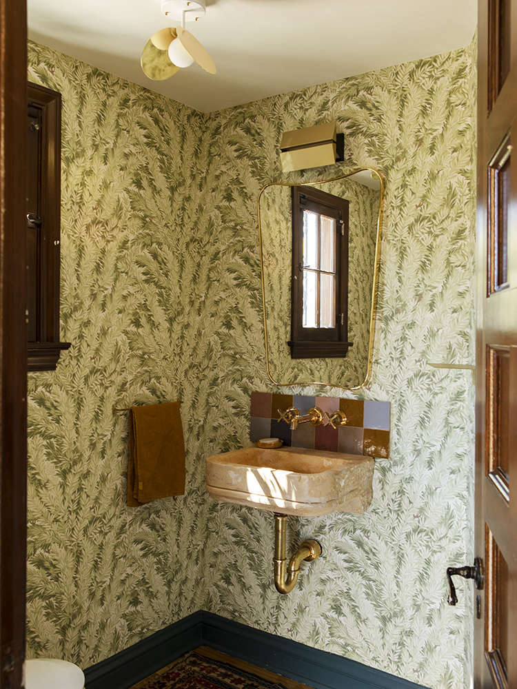 The powder room off the entry is patterned with Florencecourt, a wallpaper from the archives of Cole & Son of England. A Gio Ponti Wall Mirror hangs over a th-century Italian limestone basin. The brass ceiling fixture is from Atelier Areti and the sconce is by LA designer Brendan Ravenhill