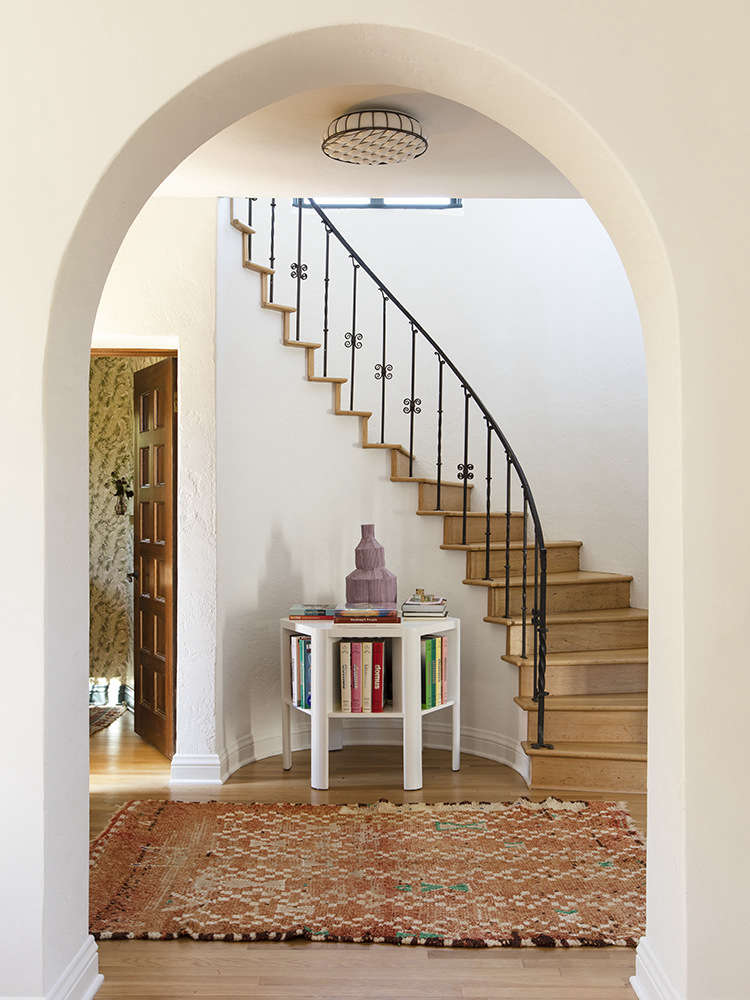 A Martin & Brocket Library Table stands in the entry under a curved stair. 