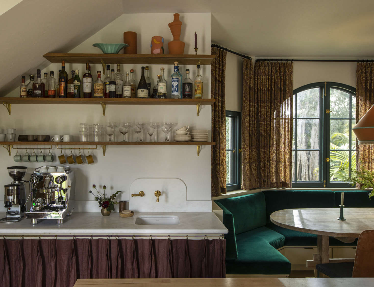 A nook with a built-in banquette upholstered in an emerald outdoor velvet from Sunbrella serves as the dining area. 