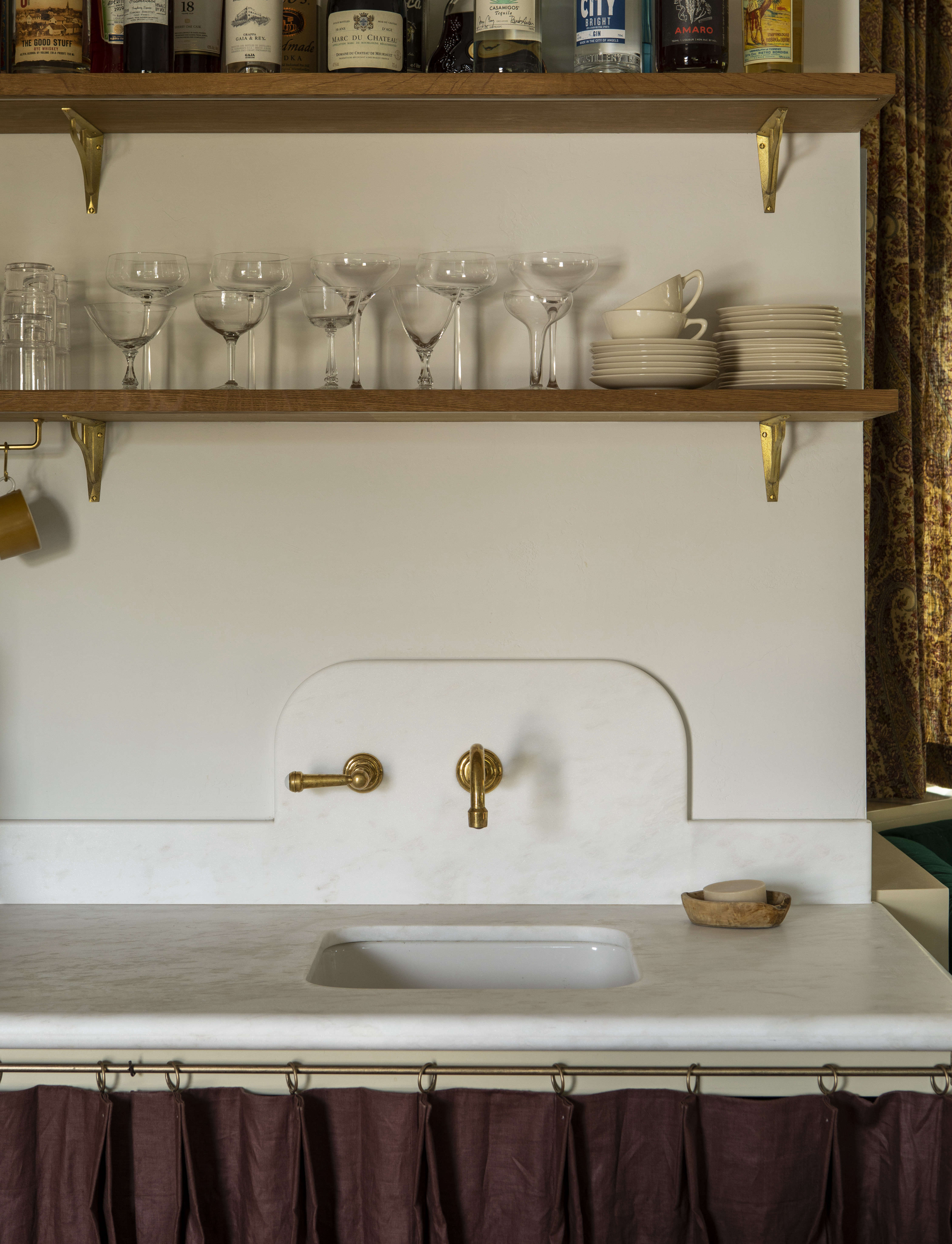 Three favorite details: the curved backsplash of Namibia White marble (with one-handle brass faucet by Watermark), bullnose-edge counter, and bar skirt of pleated plum handkerchief linen from Gray Line Linen of NYC, a notable affordable fabric source.