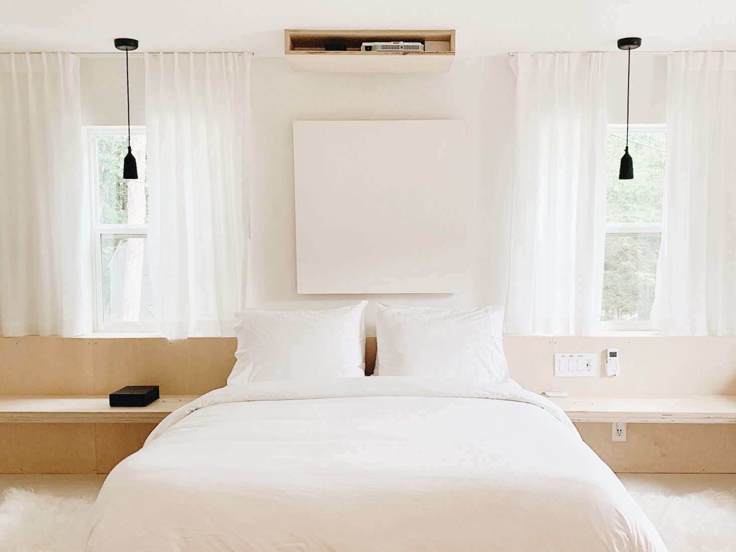 Two small upstairs bedrooms were converted to a single, airy space with windows on three sides. A built-in ledge serves as a bench and side table—Doug installed the bedside Hidden Wireless Charger marked by a circle. The couple