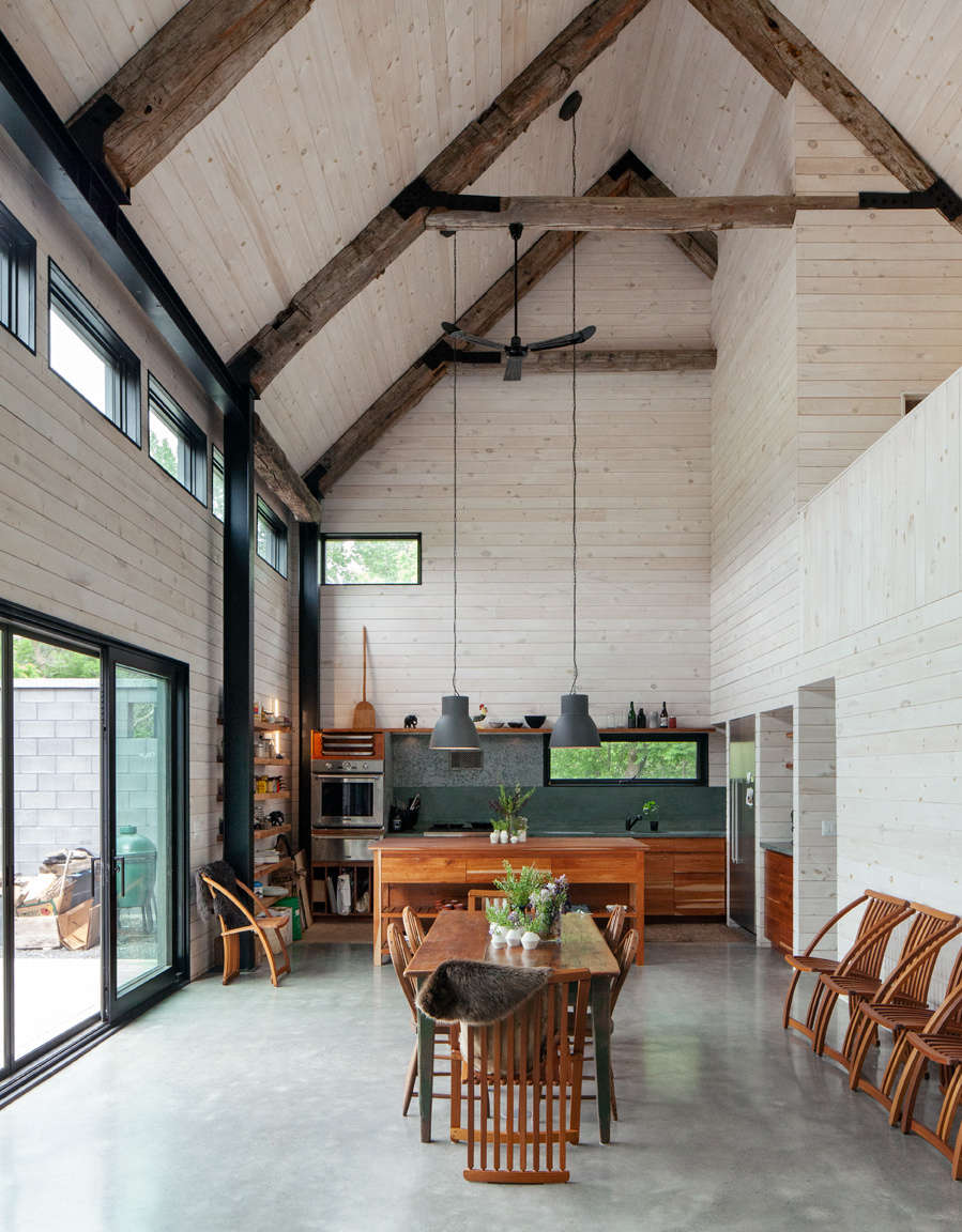 The open space in the addition features polished concrete floors, white-washed pine walls, and salvaged timber ceiling beams. The slatted dining chairs by Canadian designer Thomas Lamb were a gift from Victoria